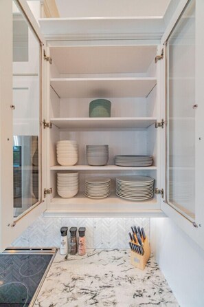 A kitchen with a built-in cabinet containing plates and bowls, a spice rack, and a knife block.