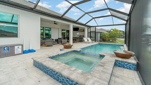 Zona de piscina exterior cubierta con jacuzzi, sillas de descanso y un patio con vistas al jardín trasero.