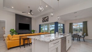 Una cocina moderna con una isla central, un comedor con mesa y sillas, un sofá y un televisor montado en la pared.