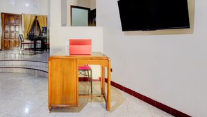 A hotel room with a wooden desk, a pink chair, a TV mounted on the wall, and a large window. - OYO 94003 Anjuk Ladang Homestay (Ngaglik)