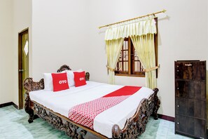 A bed with ornate wooden headboard, a red and white patterned bedspread, and two red pillows with "OYO" text. - OYO 94003 Anjuk Ladang Homestay (Ngaglik)