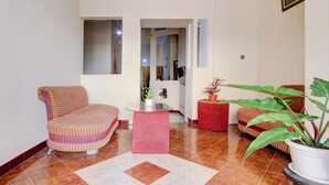 A living room with a sofa, a small table, a potted plant, and a red ottoman. - OYO 94003 Anjuk Ladang Homestay (Ngaglik)