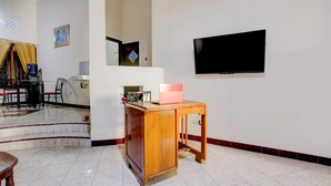 A living room with a wooden coffee table, a flat-screen TV mounted on the wall, and a dining area with chairs and a table. - OYO 94003 Anjuk Ladang Homestay (Ngaglik)