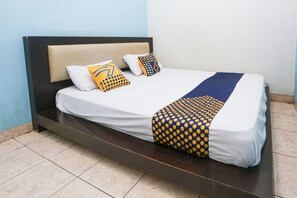 A bed with a white mattress, two pillows, a blue and yellow patterned blanket, and a dark wooden headboard. - SPOT ON 94033 Harapan Jaya (Bekasi)