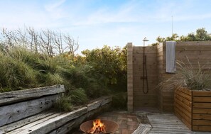 A wooden outdoor sauna with a fire pit, a wooden bench, and a wooden wall with a towel hanging.
