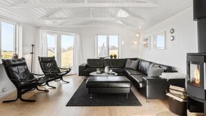 Ein modernes Wohnzimmer mit einer schwarzen Ledersofa, einem schwarzen Ledersessel, einem runden Couchtisch und einem Kaminofen.