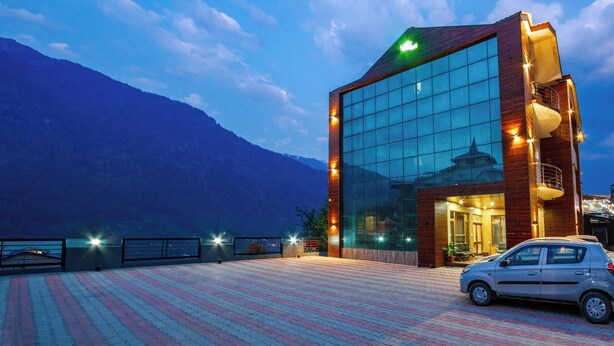 A modern building with a glass facade, a car parked in front, and a mountainous backdrop. - Foxoso Cherry Hotel Manali (Manali)
