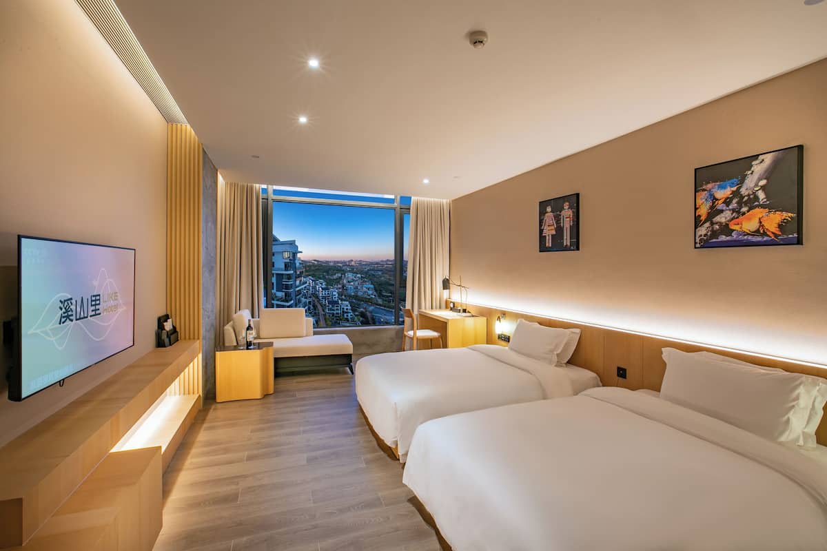 Une chambre d’hôtel avec deux lits, une télévision, un bureau et une grande fenêtre donnant sur la ville.
