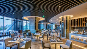 Un restaurant moderne doté d’un haut plafond, de grandes fenêtres et d’une colonne centrale. Les tables et les chaises sont disposées pour accueillir les clients.