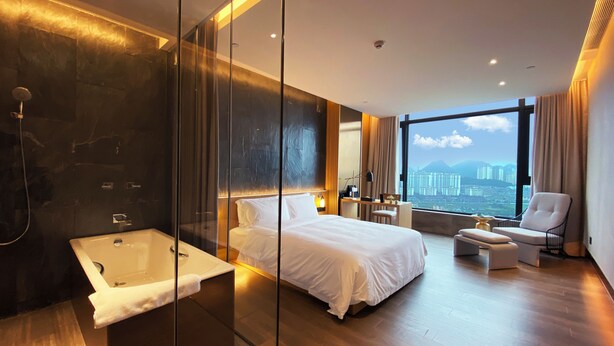 Une chambre d’hôtel moderne dotée d’un grand lit, d’une douche séparée, d’un bureau et offrant une vue sur le paysage urbain.