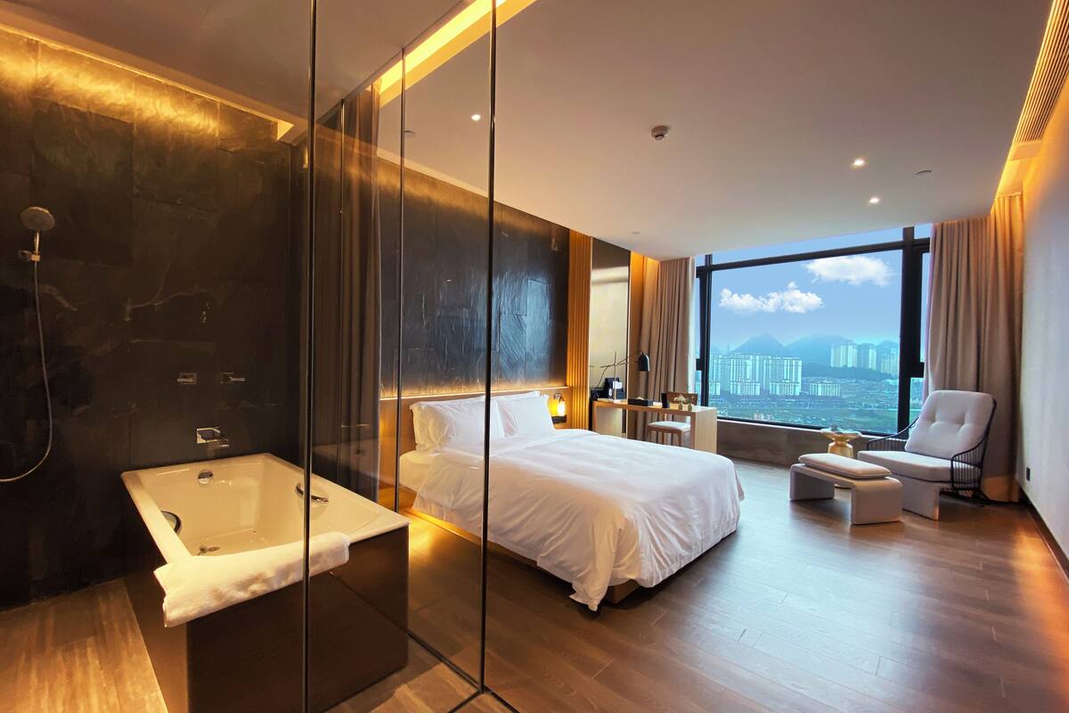 Une chambre d’hôtel moderne dotée d’un grand lit, d’une douche séparée, d’un bureau et offrant une vue sur le paysage urbain.