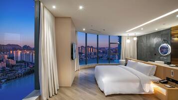 Una habitación de hotel moderna con una cama grande, un baño con espejo y vistas a la ciudad a través de amplias ventanas.