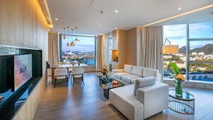 Une chambre d’hôtel moderne dotée d’une grande fenêtre donnant sur la ville, d’un téléviseur à écran plat, d’un canapé, d’un coin repas et d’une petite table agrémentée d’un vase de fleurs.