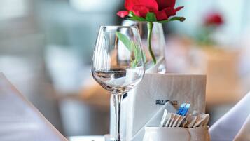Una mesa de comedor con una copa de vino, un florero con una rosa roja y un portavasos.