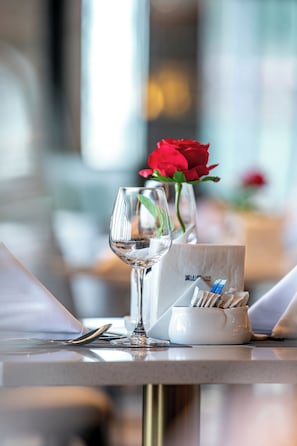 Une table à manger avec un verre à vin, un vase contenant une rose rouge et un porte-serviettes.