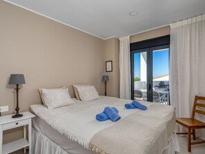Une chambre d’hôtel avec un grand lit, deux lampes de chevet, une chaise en bois et une vue sur l’extérieur grâce à une porte coulissante.