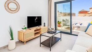 Ein modernes Wohnzimmer mit Fernseher, Holzmöbeln, einem Glastisch und einem Balkon mit Sitzgelegenheit.