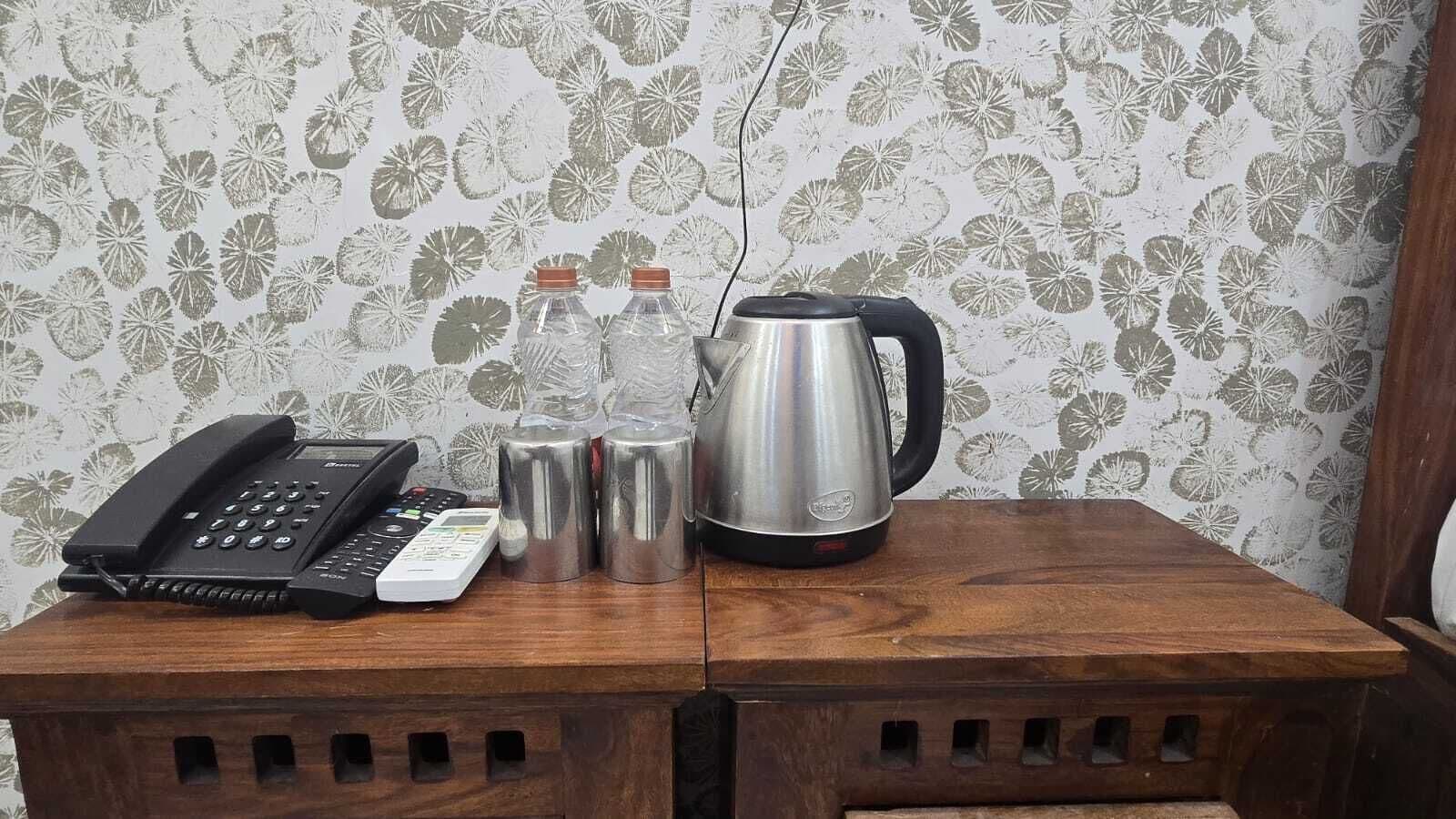 Una mesa de madera con un teléfono, dos termos y un hervidor.