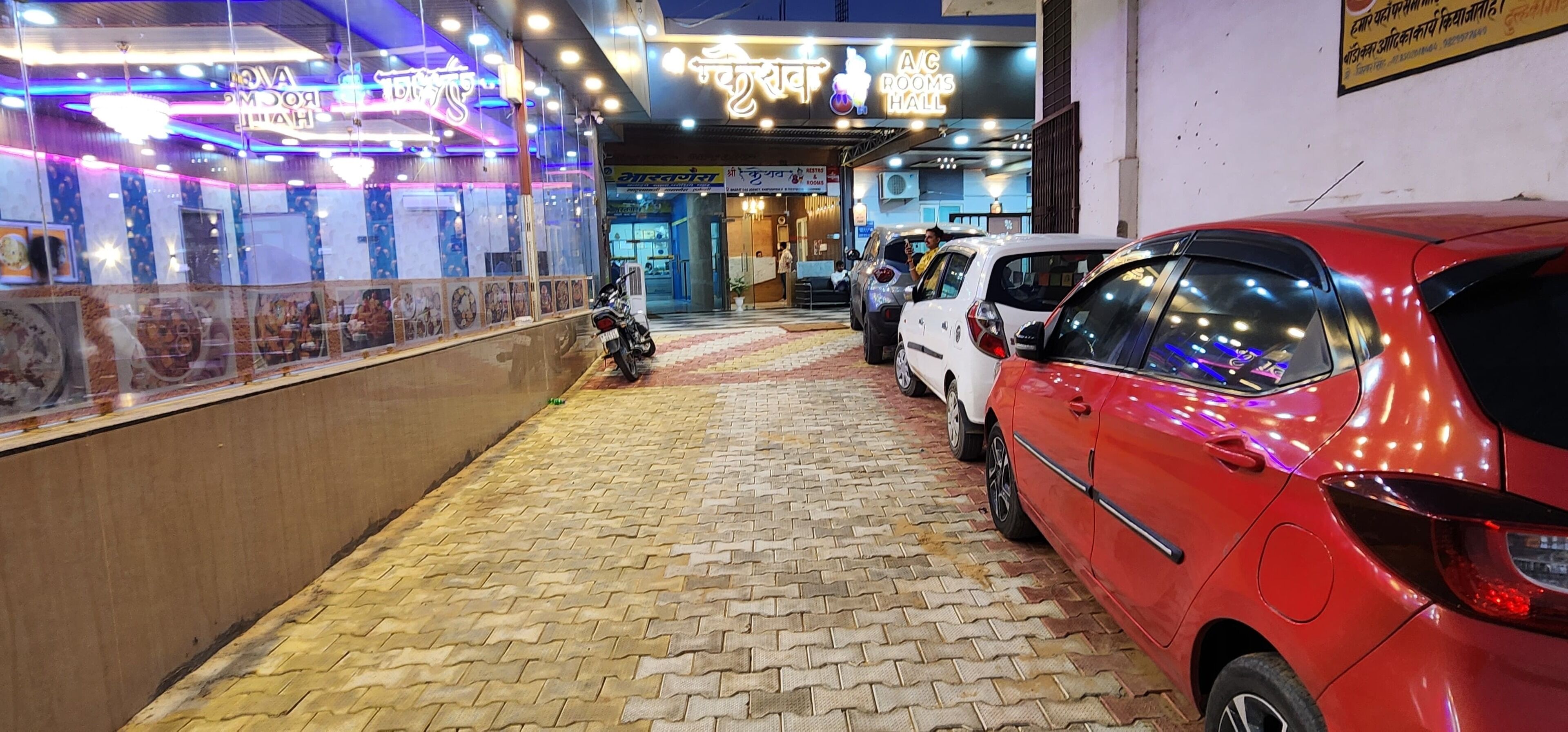 L'ingresso di un hotel con pavimento piastrellato, una motocicletta parcheggiata all'esterno e un'auto rossa parcheggiata a destra.