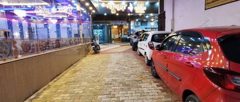 L'ingresso di un hotel con pavimento piastrellato, una motocicletta parcheggiata all'esterno e un'auto rossa parcheggiata a destra.