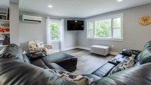 A living room with leather sofas, a flat-screen TV, and a large window. - Boondock Retreat, pet friendly 4 bedroom home with EV charger (Himrod)