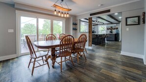 A dining area with a wooden table and chairs, a hanging light fixture, and a view through large windows. - Boondock Retreat, pet friendly 4 bedroom home with EV charger (Himrod)