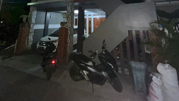 Ein zweistöckiges Gebäude mit Garage, Treppe und einem abgestellten Motorrad.