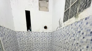 Ein kleines Badezimmer mit Toilette, einem roten Eimer und gefliesten Wänden.