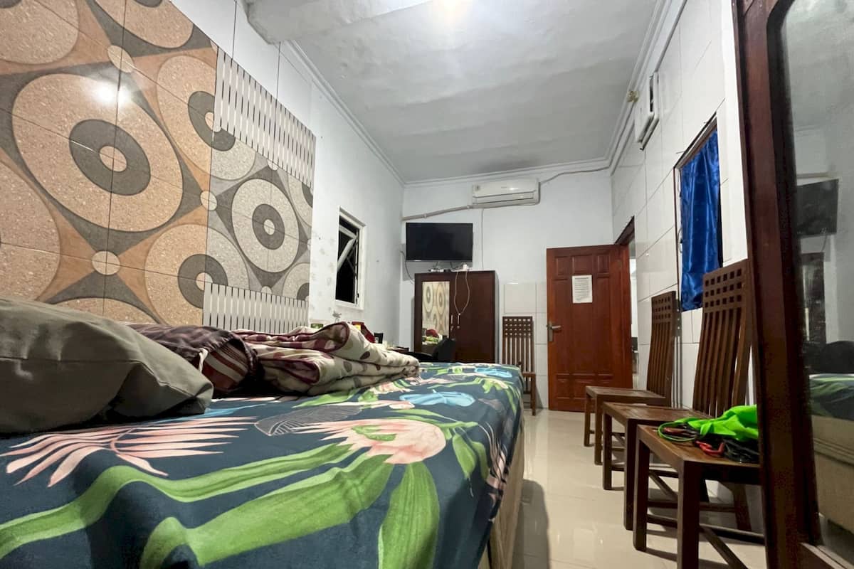 A bedroom with a bed, a desk, and a chair. There is a window with a blue curtain, a door, and a wall-mounted TV.