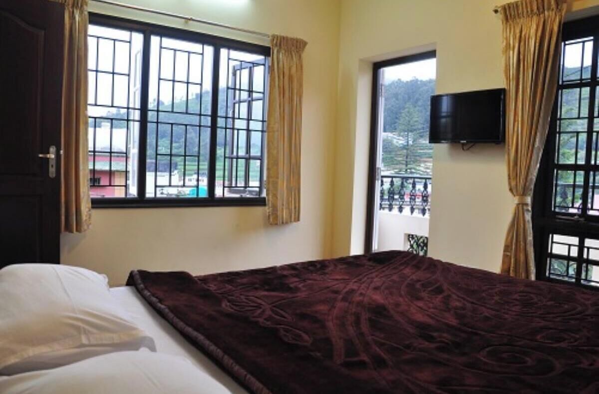Habitación de hotel con cama, televisión montada en la pared y ventana con cortinas.