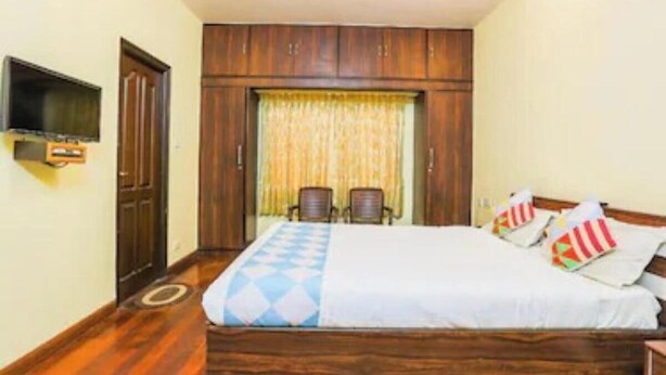 A bedroom with a bed, a television, a wardrobe, and a window with curtains. - Silver Spring Cottages (Ootacamund)