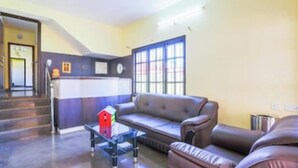 A reception area with a sofa, a small table, and a window with blinds. - Silver Spring Cottages (Ootacamund)