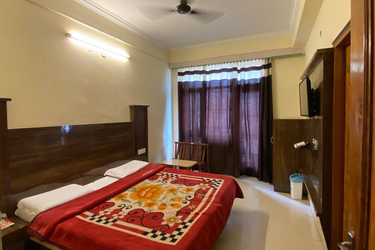 Habitación de hotel con una cama grande, cabecera de madera, escritorio y una silla. Se ve una ventana con cortinas y un ventilador de techo.