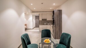 A modern kitchen with a central island, a dining area with a glass table, and green upholstered chairs. - juSTa Residences - AIPL Joy Street Gurgaon (Gurugram)