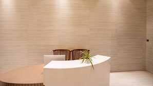 A modern, minimalist conference room with a curved white table, two wooden chairs, and a potted plant. - juSTa Residences - AIPL Joy Street Gurgaon (Gurugram)