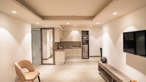 A modern living room with a flat-screen TV, a comfortable armchair, and a wooden entertainment unit. - juSTa Residences - AIPL Joy Street Gurgaon (Gurugram)