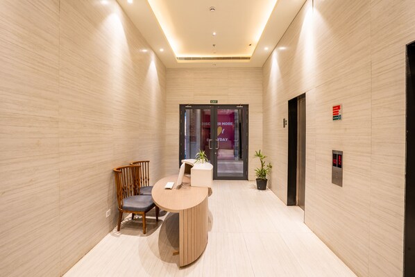 Un moderno hall de hotel con una recepción, una silla de madera, una planta en maceta y un ascensor.