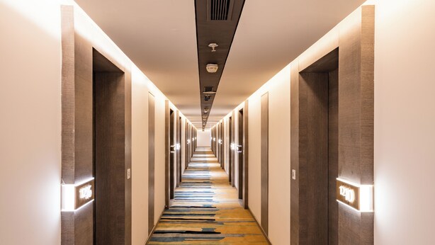 A hotel corridor with a patterned carpet, recessed lighting, and a series of doors on either side. - juSTa Residences - AIPL Joy Street Gurgaon (Gurugram)