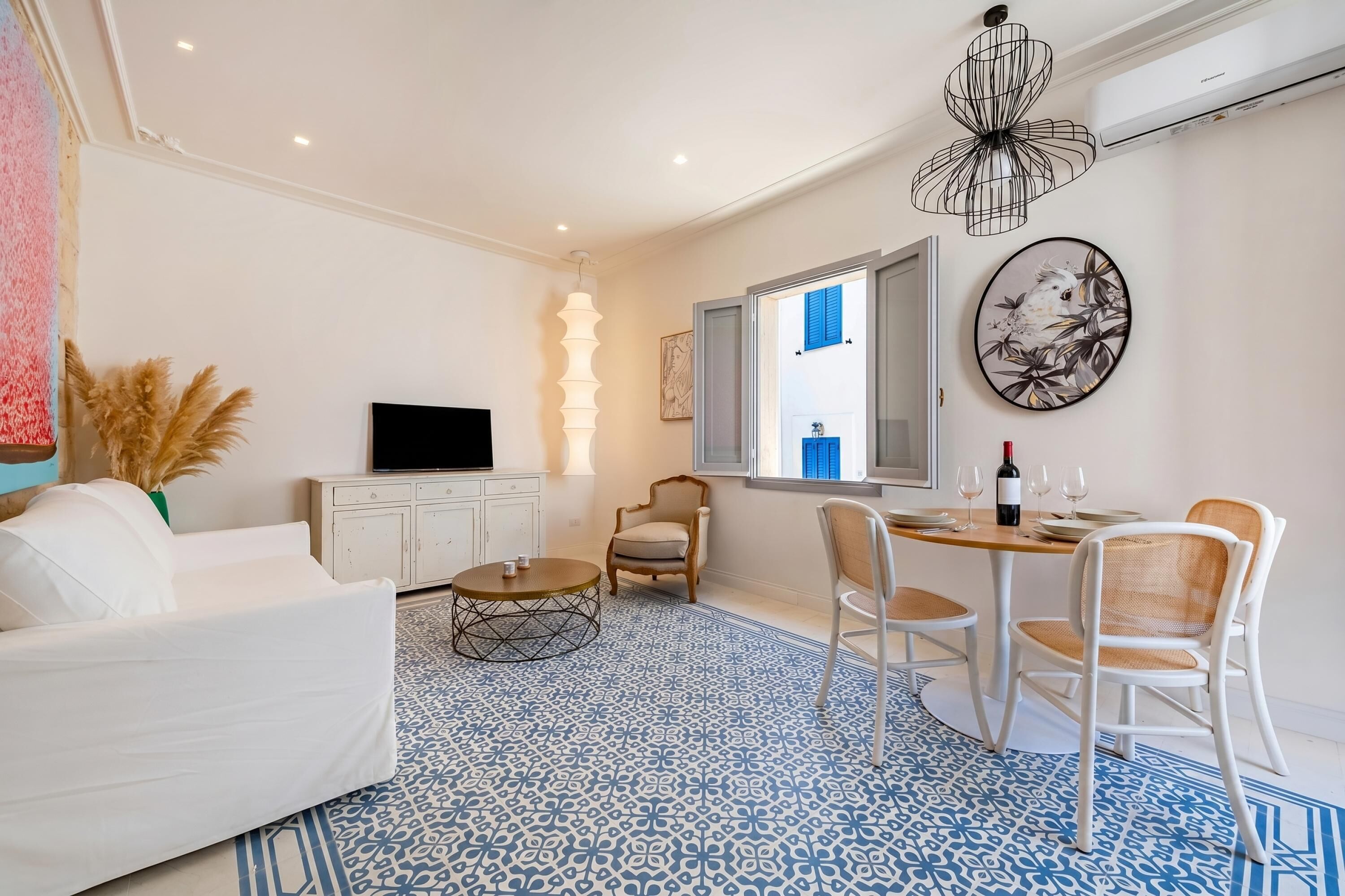 Un salon moderne comprenant un canapé, un téléviseur, une table à manger, des chaises et un tapis à motifs.