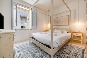 A four-poster bed with white linens, a bedside table with a lamp, a painting on the wall, and a patterned floor. - Dimora del Levante Monopoli (Monopoli)