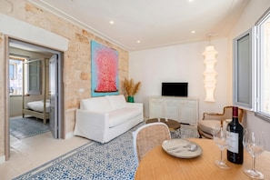 A modern living room with a white sofa, a dining table with chairs, a TV, and a wine bottle. - Dimora del Levante Monopoli (Monopoli)