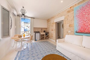A living room with a white sofa, a dining table with chairs, a kitchen area, and a patterned rug. - Dimora del Levante Monopoli (Monopoli)