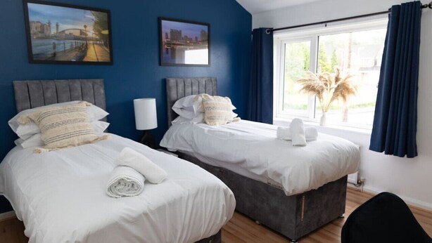 A hotel room with two beds, a large window with curtains, and artwork on the walls.