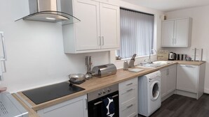 A compact kitchen with white cabinets, a built-in oven, a washing machine, and a toaster.