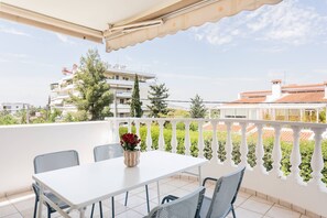 A balcony with a white table and chairs, a potted plant, and a view of buildings and trees. - Spacious Serenity in Marousi (Marousi)