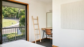A room with a bed, a desk with a chair, a ladder, and a large window overlooking a road and greenery. - Pet-friendly 2 bedroom villa (Lennox Head)