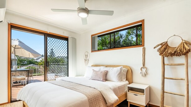 A bedroom with a bed, a nightstand, a wall-mounted lamp, a ladder, and a view of the outdoors. - Pet-friendly 2 bedroom villa (Lennox Head)