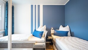 A bedroom with two beds, each with white bedding and blue pillows, against a blue wall. - Barby apartment with Elbe view & balcony on the Elbe-Saale Cycle Path (Barby (Elbe))