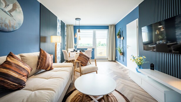 A modern living room with a sofa, armchair, and coffee table, a dining area with chairs, and a TV mounted on the wall. - Barby apartment with Elbe view & balcony on the Elbe-Saale Cycle Path (Barby (Elbe))