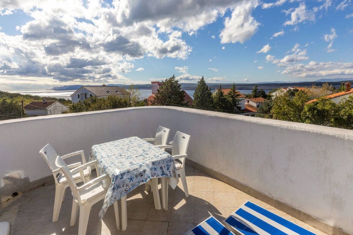 Una terraza con mesa y sillas, vistas al mar y edificios, y un cielo parcialmente nublado.